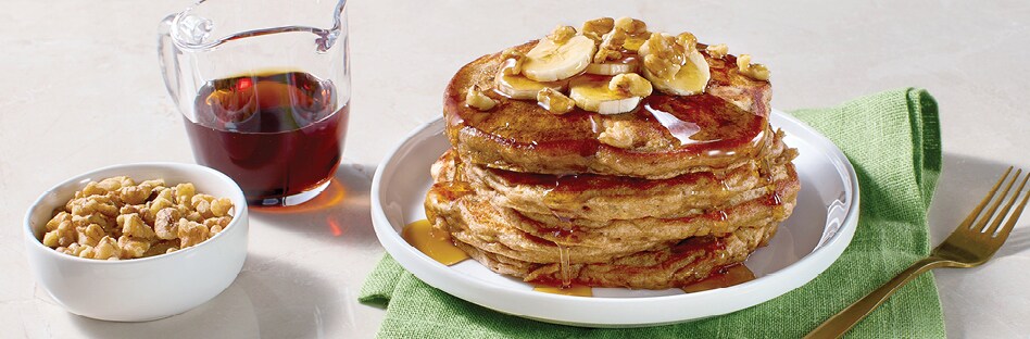  A stack of banana-walnut pancakes topped with banana slices, walnuts and maple syrup.