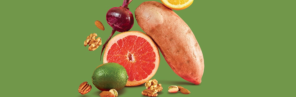 Citrus fruits, root vegetables, and nuts on a green background