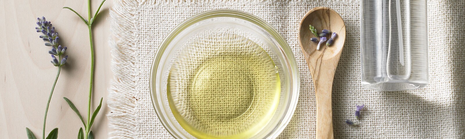 A bowl full of oil atop a linen cloth surrounded by rosemary, clove, eucalyptus herbs and essential oils 