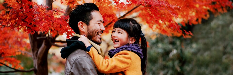 Dad and daughter smiling with fall trees in background