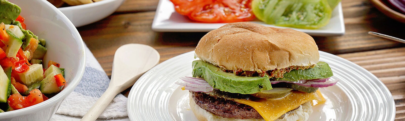 A burger loaded with toppings sits on a white plate surrounded by various burger topping ingredients A burger loaded with toppings sits on a white plate surrounded by various burger topping ingredients