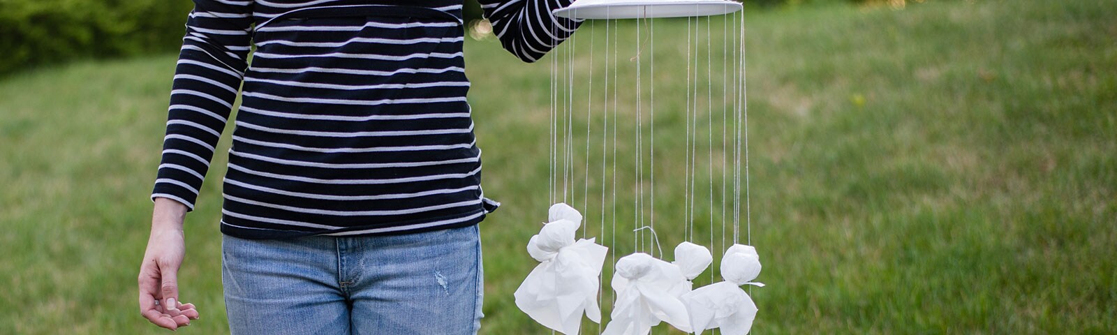 Woman holding a homemade mobile with multiple tissue ghosts hanging from a plate Woman holding a homemade mobile with multiple tissue ghosts hanging from a plate