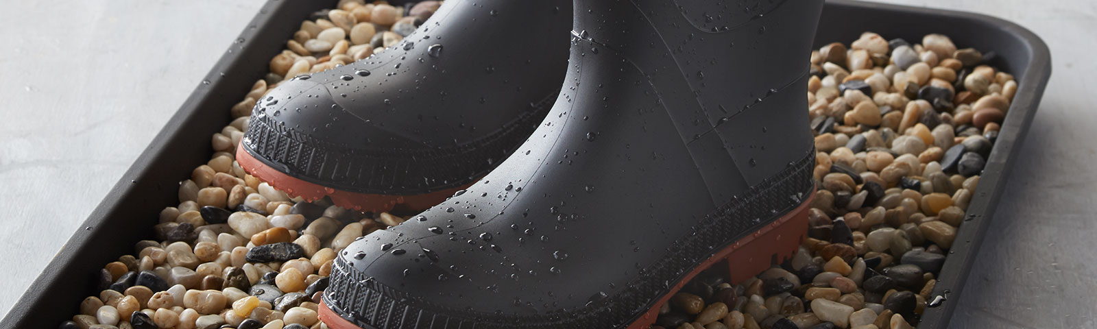 Wet rain boots atop a bed of pebbles sitting in a tray Wet rain boots atop a bed of pebbles sitting in a tray