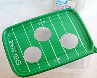 Decorated green rectangle container lid with 50-yard line and end zones drawn in white marker Decorated green rectangle container lid with 50-yard line and end zones drawn in white marker