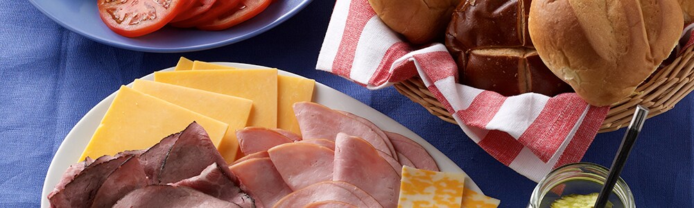Meats and cheeses, hamburger buns and veggie toppings on a platter
