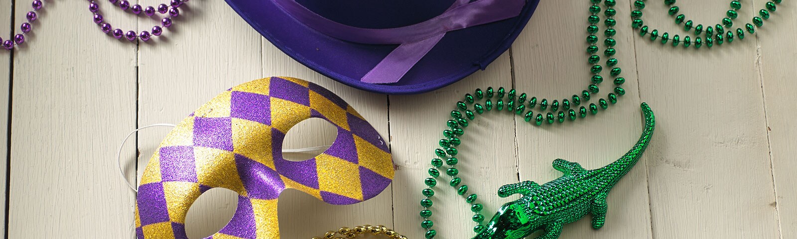 Mardi Gras beads, masks, and hats on a white painted wooden table Mardi Gras beads, masks, and hats on a white painted wooden table