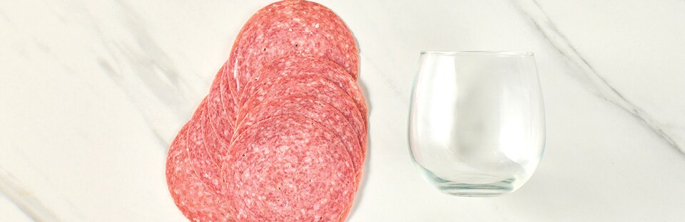 Stack of salami slices with wine glass on a white marble surface