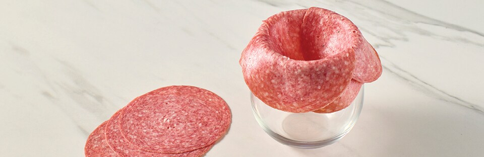 Multiple salami slices layered over wine glass rim